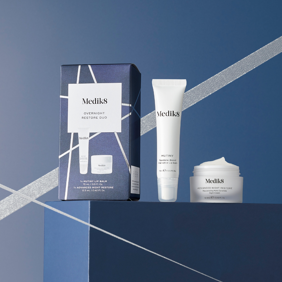 Medik8 Overnight Restore Duo includes Mutiny Lip Balm 15ml and Advanced Night Restore 12.5ml, both stored in white containers, and dark blue box with silver accents.